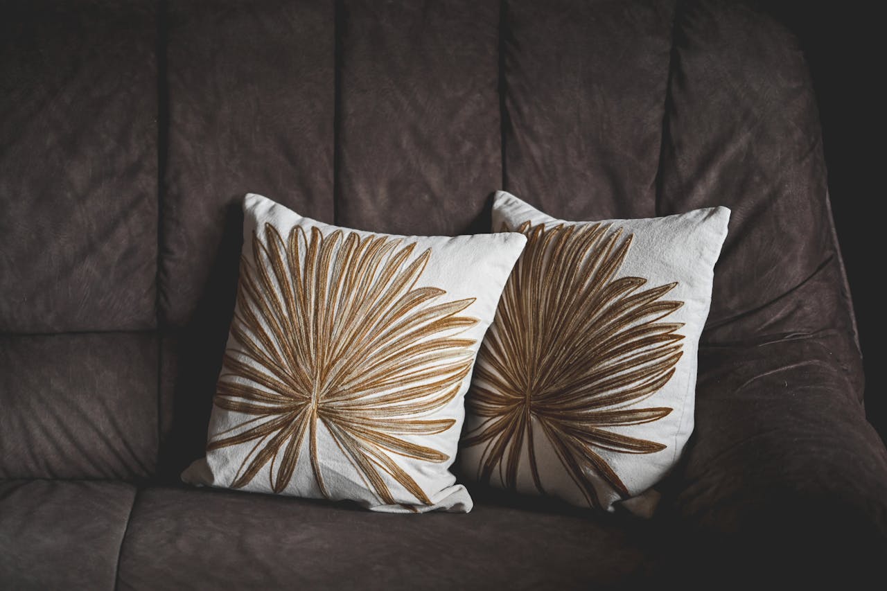 services-04 Pair of decorative pillows with leaf patterns on a brown sofa, creating a stylish home interior look.