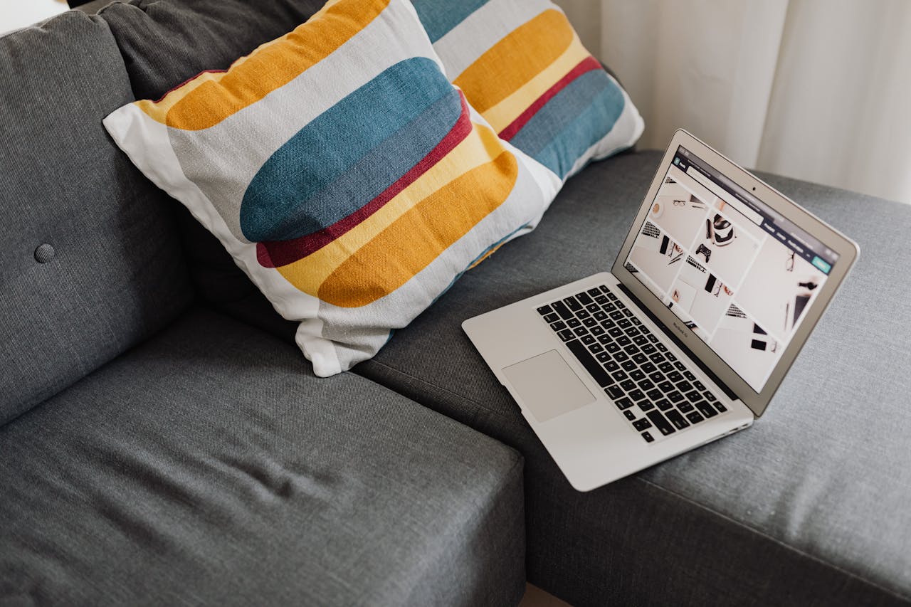 Elegant gray sofa setup with a laptop and colorful throw pillows for a cozy workspace.