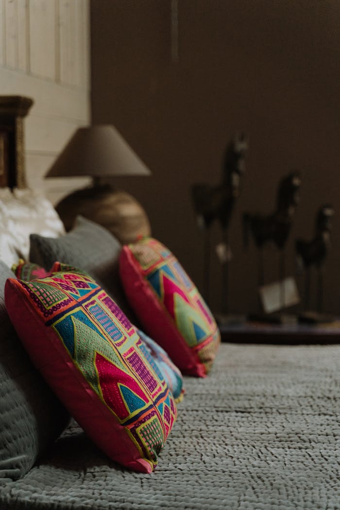 Stylishly arranged colorful throw pillows on a cozy bed with lamps and decor in a warm-toned room.