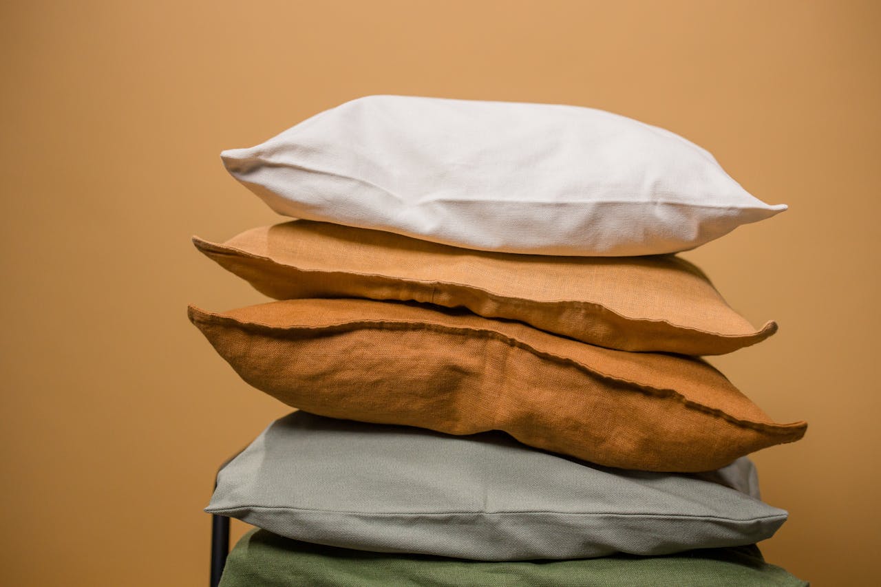 home-hero Stack of different colorful pillows folded and placed in stack on chair isolated on dark beige background